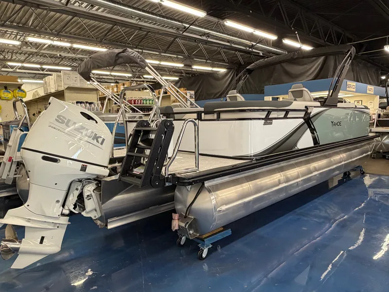The Image of A 2026 Tahoe LTZ 2385 QL pontoon boat with a Suzuki outboard motor in a showroom. - 0
