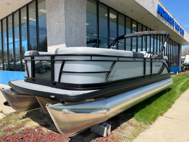Slide: The Image of A modern pontoon boat with a gray hull and black railing, parked outside a building. - 1