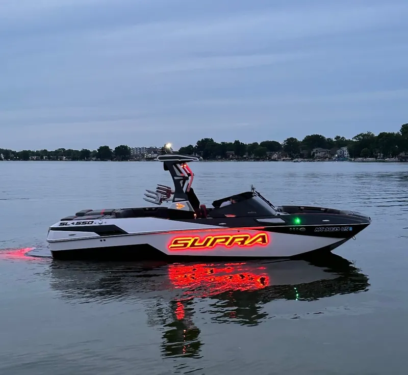 Slide: The Image of A 2022 Skiers Choice SL 550 boat on calm water, featuring a glowing "SUPRA" logo. - 16