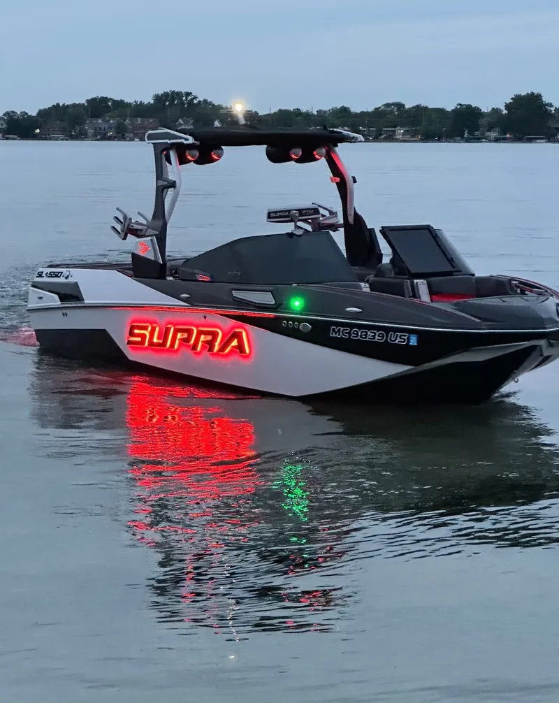 Slide: The Image of A 2022 Skiers Choice SL 550 boat with glowing "Supra" lettering on calm water. - 18