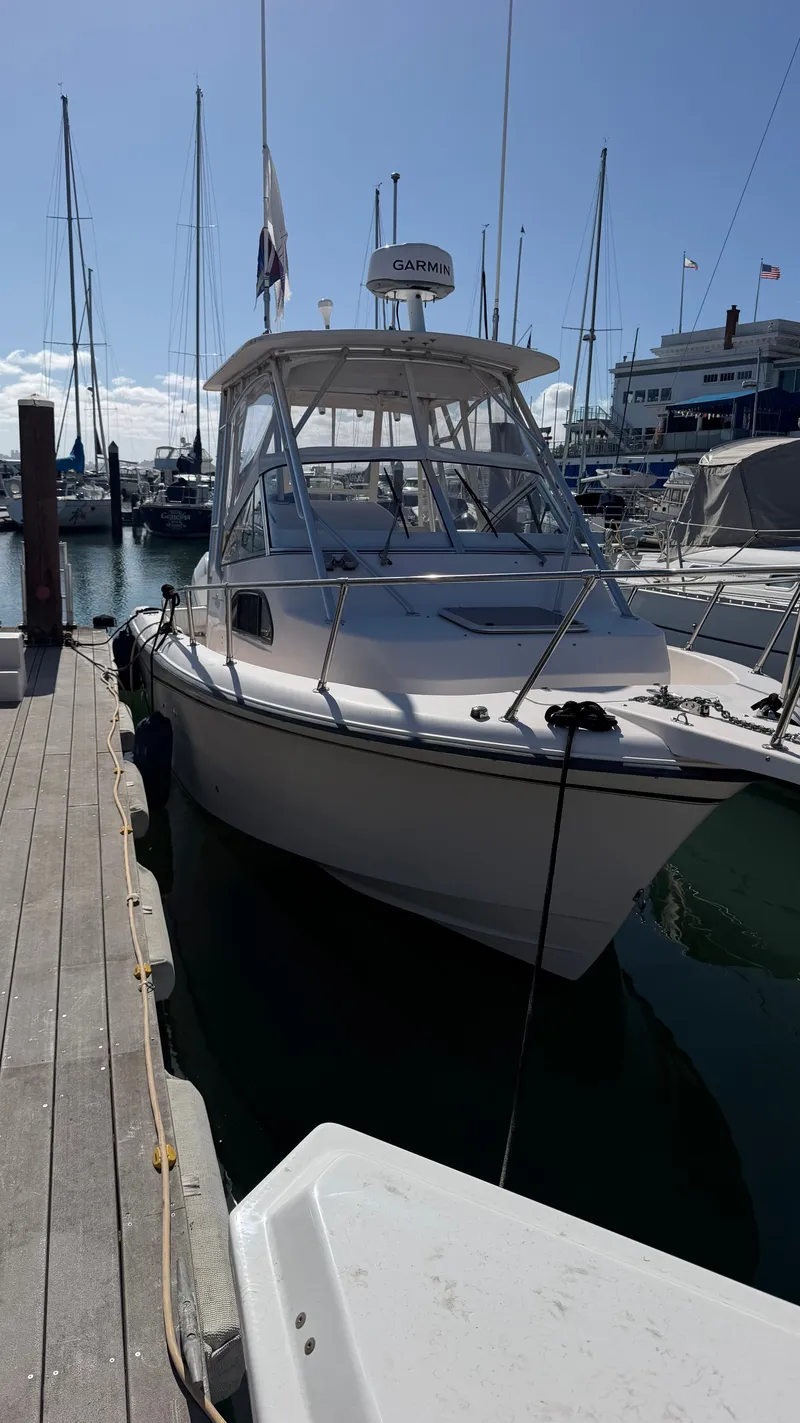 The Image of A 2002 Grady-White Sailfish 282 docked at a marina. It features an enclosed helm and is surrounded by other boats. - 0