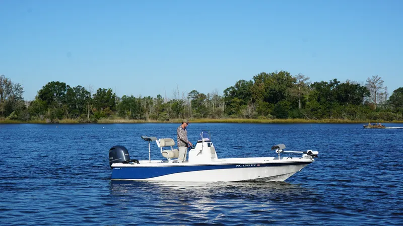 Slide: The Image of A man stands on a blue and white boat on a calm lake. - 1