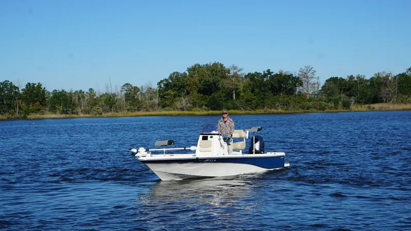 Slide: The Image of A man navigates a blue and white boat on a calm lake with a wooded shoreline. - 5