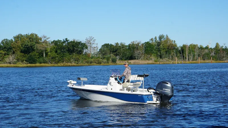 Slide: The Image of A man operates a blue and white boat on a calm lake with a wooded shoreline. - 6