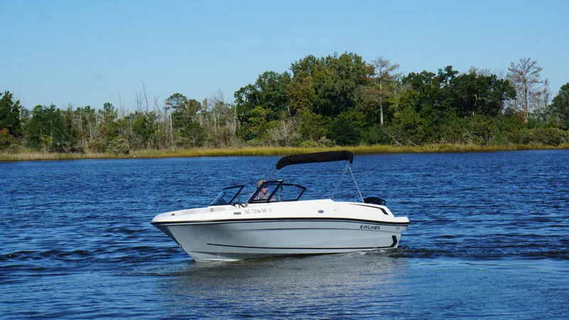 Slide: The Image of Bayliner VR4 Bowrider OB 2025 on a calm lake with a wooded shoreline in the background. - 1