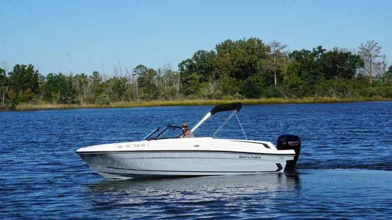Slide: The Image of 2025 Bayliner VR4 Bowrider OB on calm water with a wooded shoreline in the background. - 2