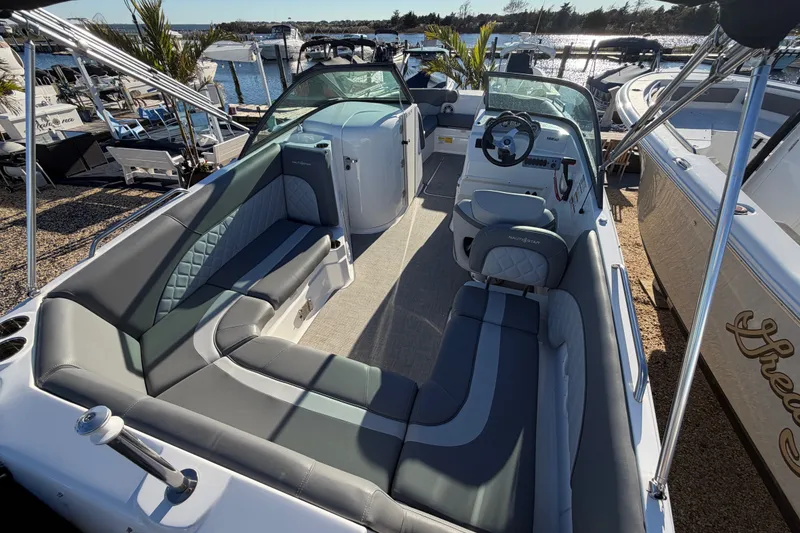 Slide: The Image of 2024 NauticStar 223 DC Deck boat interior with seating and steering wheel, docked by the water. - 6