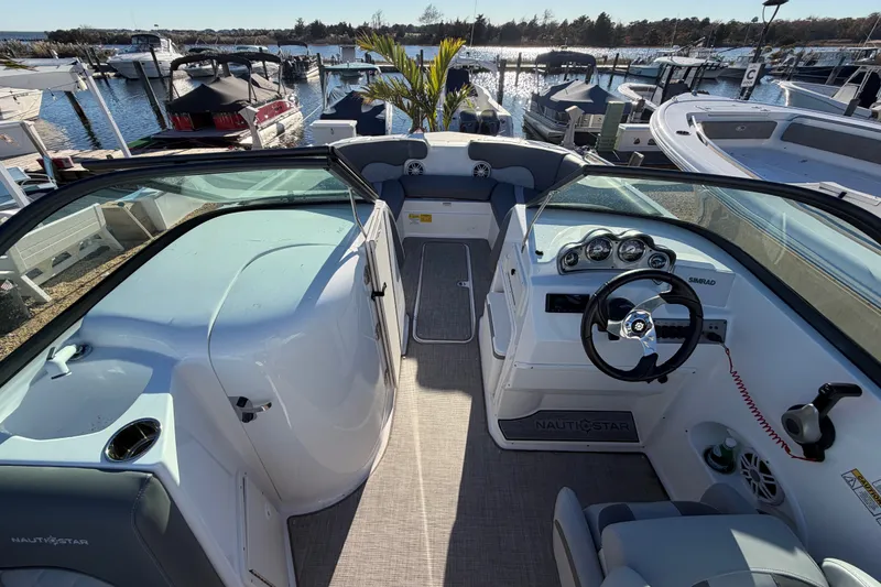 Slide: The Image of 2024 NauticStar 223 DC Deck boat interior with steering wheel and dashboard, docked at marina. - 16