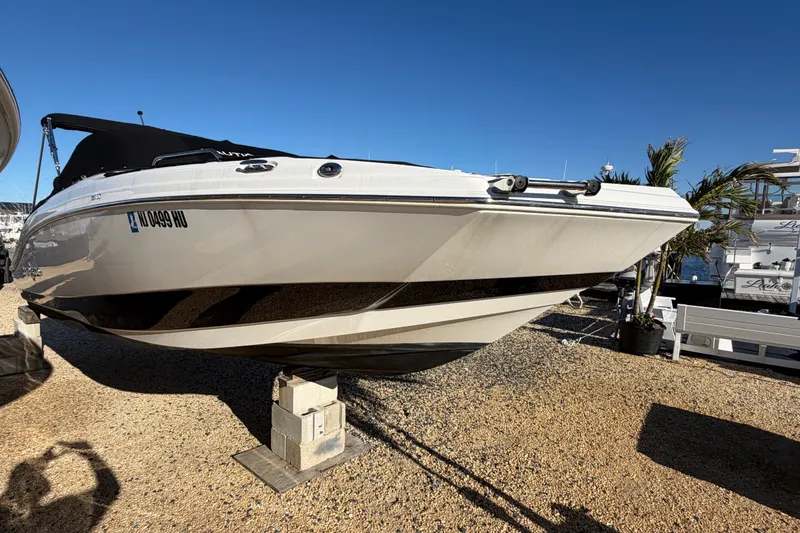 The Image of 2024 NauticStar 223 DC Deck boat on display, elevated on blocks, under clear blue sky. - 0