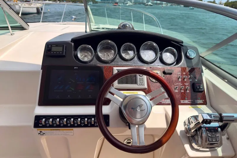 Slide: The Image of 2013 Sea Ray Sundancer 310 helm with gauges, steering wheel, and control panel on water. - 7