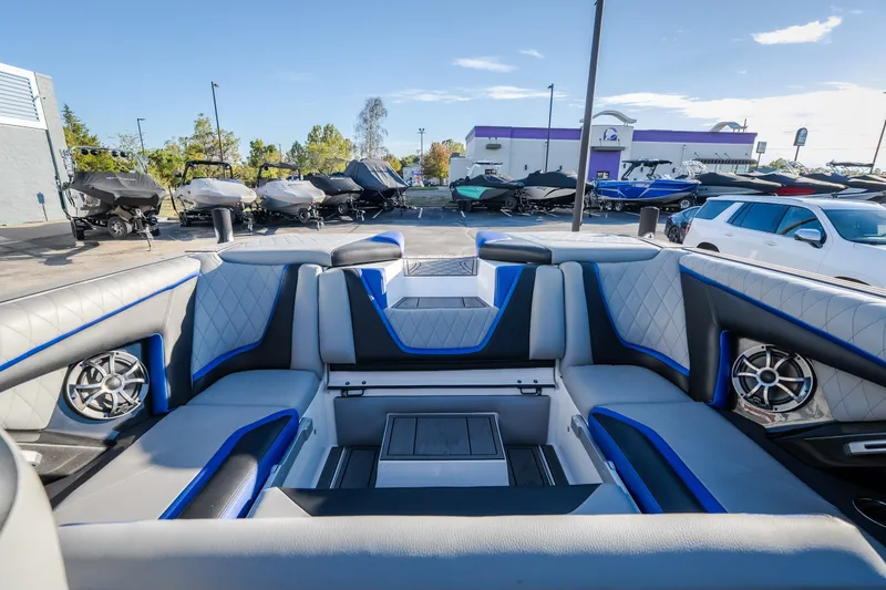 Slide: The Image of 2018 Tigé RZX3 boat interior with blue and gray seating, parked among other boats. - 16