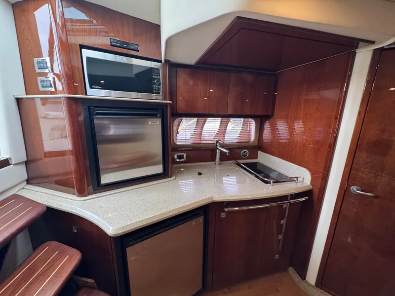 Slide: The Image of The 2010 Sea Ray 390 Sundancer galley features glossy wood cabinets, a sink, and modern appliances. - 26