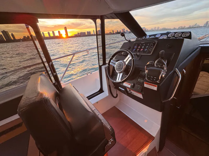 Slide: The Image of The cockpit of a 2017 Jeanneau NC 11 with a view of the sunset over the city. - 40
