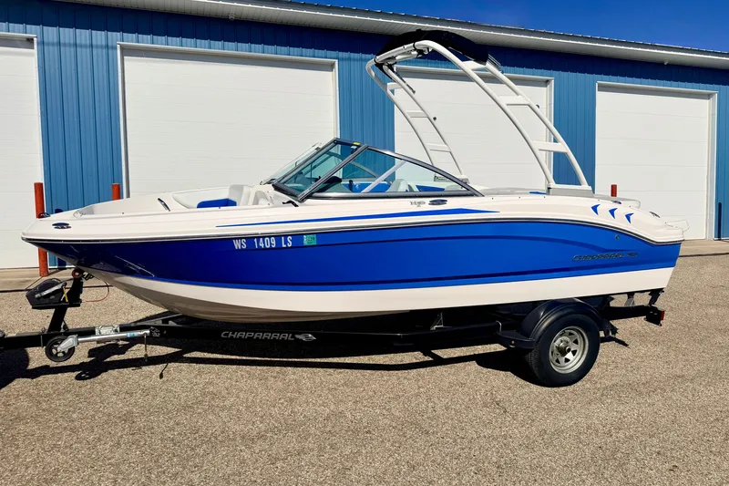 Slide: The Image of 2017 Chaparral 19 Sport H2O boat in blue and white, parked on a trailer. - 2