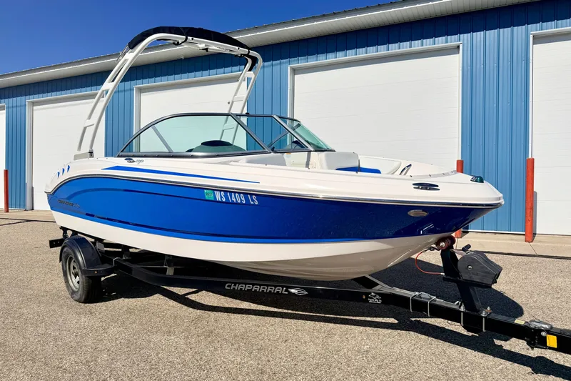 Slide: The Image of 2017 Chaparral 19 Sport H2O boat on trailer, blue and white, parked outside a blue building. - 6