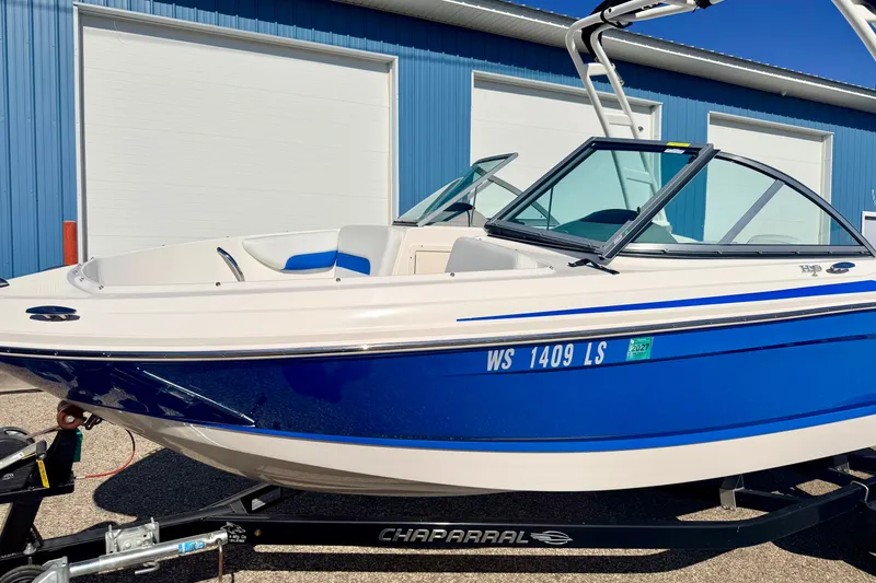 Slide: The Image of 2017 Chaparral 19 Sport H2O boat in blue and white, parked outside a blue building. - 12