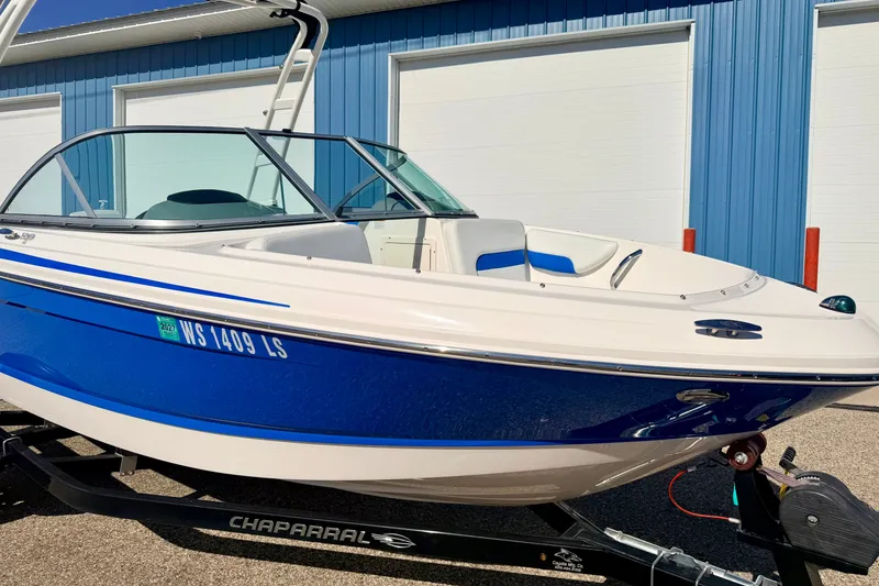 Slide: The Image of 2017 Chaparral 19 Sport H2O boat with blue and white design, parked near blue building. - 17