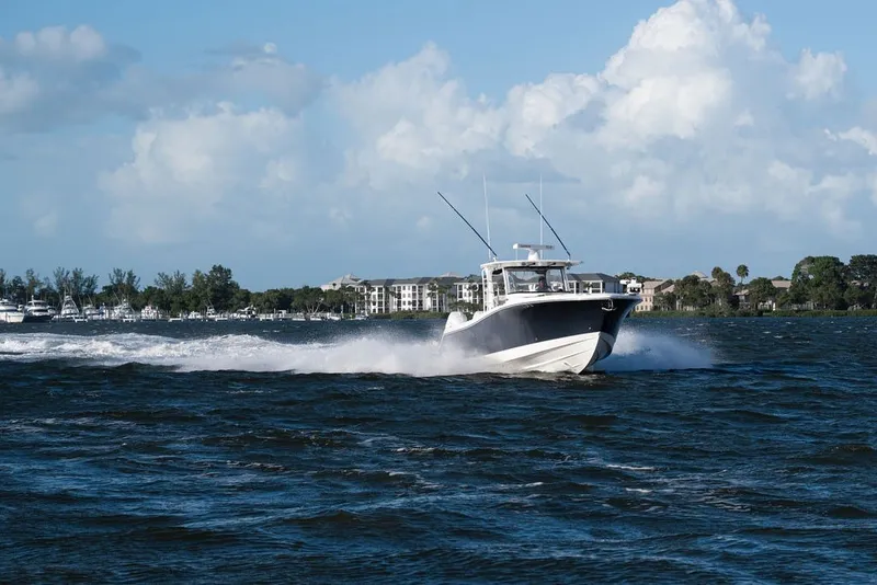 Slide: The Image of 2020 Edgewater 370CC boat cruising on a sunny day with coastal buildings in the background. - 8