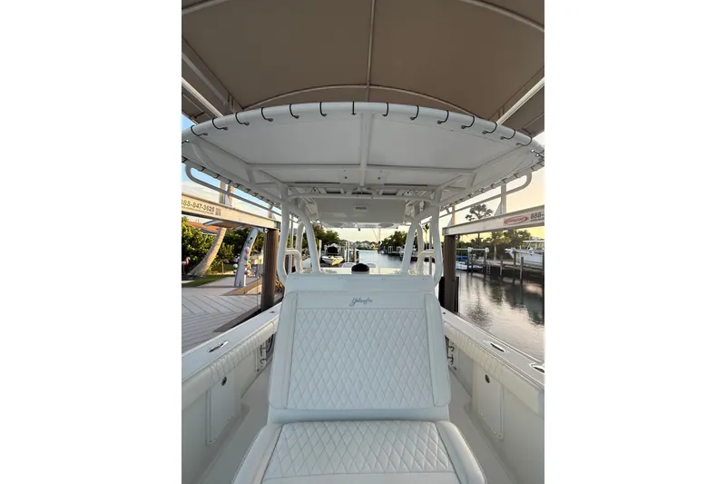 Slide: The Image of 2014 Yellowfin 32 Offshore boat interior with white seating and canopy, docked by a serene waterfront. - 14