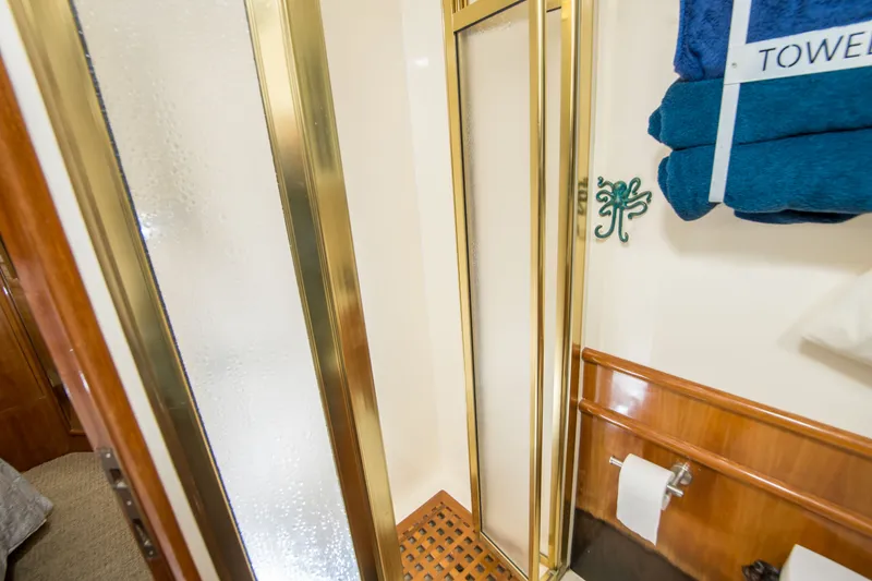 Slide: The Image of Luxurious bathroom with gold-framed shower, blue towels, and wooden accents on a 2000 Johnson 58 yacht. - 13