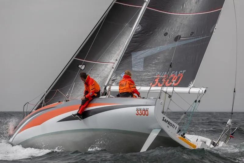 Slide: The Image of 2025 Jeanneau Sun Fast 3300 sailing on open water, crew in orange gear. - 32
