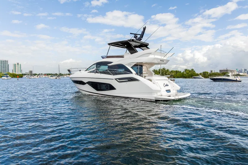 Slide: The Image of 2023 Sunseeker Manhattan 55 yacht cruising on a scenic waterway under a partly cloudy sky. - 12