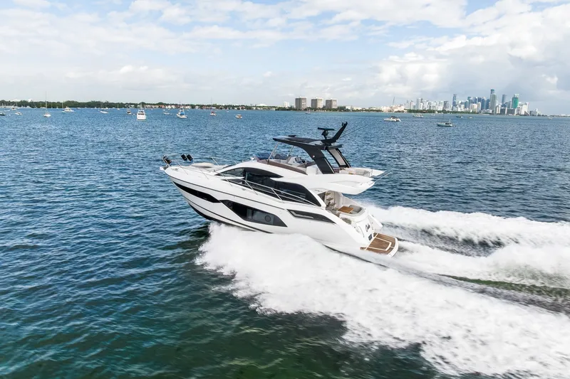 Slide: The Image of 2023 Sunseeker Manhattan 55 yacht cruising on open water with city skyline backdrop. - 10