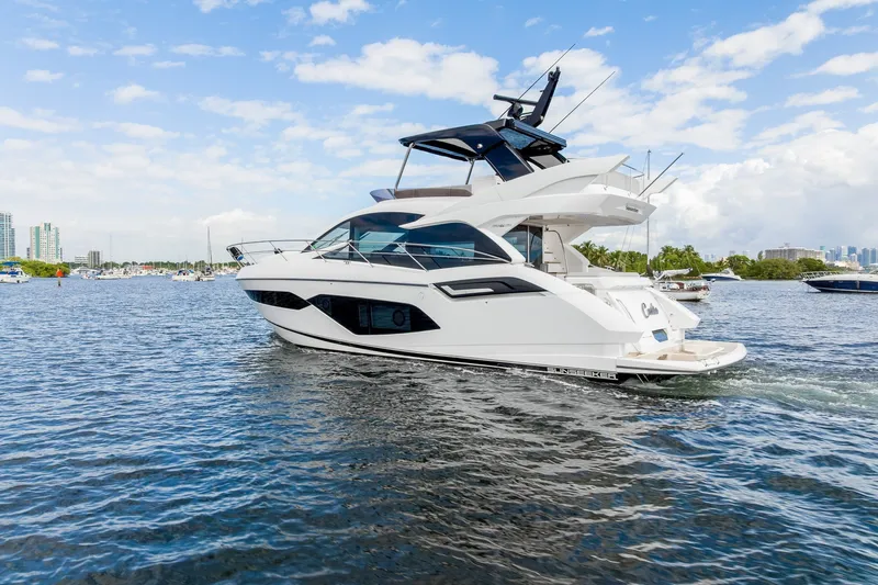 Slide: The Image of 2023 Sunseeker Manhattan 55 yacht cruising on a sunny day, with city skyline in background. - 13