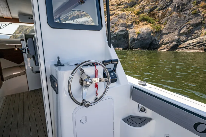 Slide: The Image of Helm of 2025 Ocean Sport 27 boat with scenic rocky shoreline background. - 18