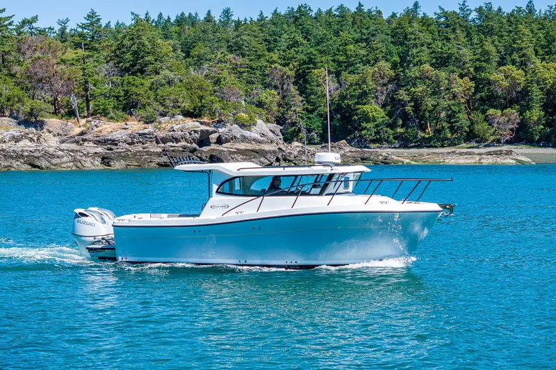 Slide: The Image of 2025 Ocean Sport 27 boat cruising on clear blue water near a forested shoreline. - 27