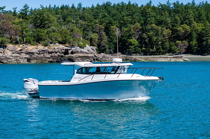 Slide: The Image of Ocean Sport 27 boat cruising on blue water near a forested shoreline, 2025 model. - 28