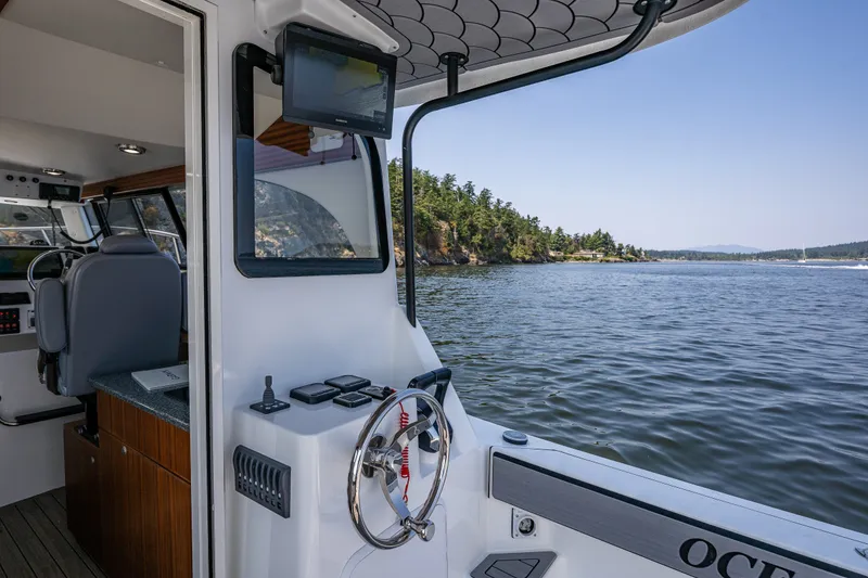 Slide: The Image of 2025 Ocean Sport 27 boat interior with steering wheel, navigation screen, and scenic water view. - 17