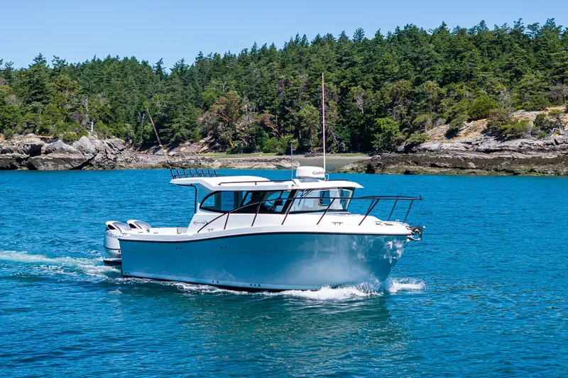 The Image of 2025 Ocean Sport 27 boat cruising on clear blue water near a forested shoreline. - 0