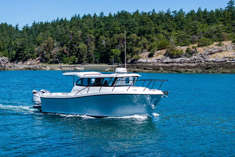 Slide: The Image of 2025 Ocean Sport 27 boat cruising on clear blue water near a forested shoreline. - 31