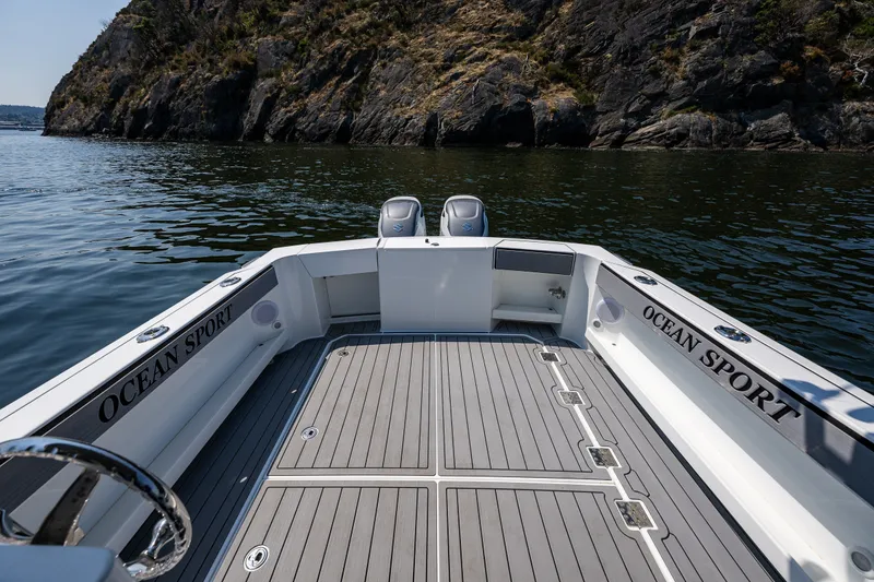 Slide: The Image of 2025 Ocean Sport 27 boat with spacious deck, dual engines, near rocky shoreline. - 16