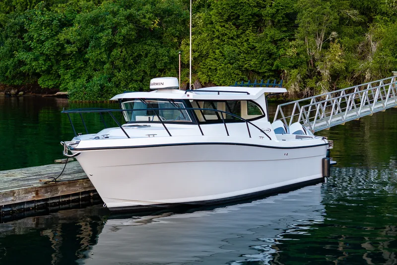 Slide: The Image of 2025 Ocean Sport 27 boat docked by lush greenery and calm water. - 35