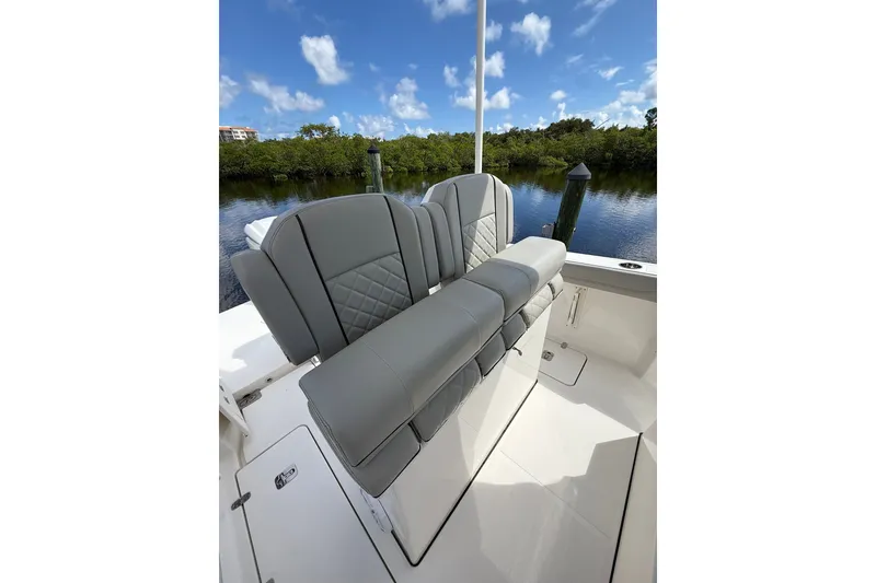 Slide: The Image of 2023 Pursuit S 248 Sport boat seating with gray upholstery, docked by a scenic waterway. - 11