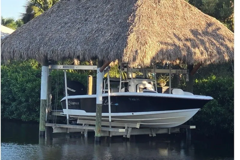 The Image of A 2015 Crevalle 23 Bay boat under a thatched roof, on a boat lift above the water. - 2