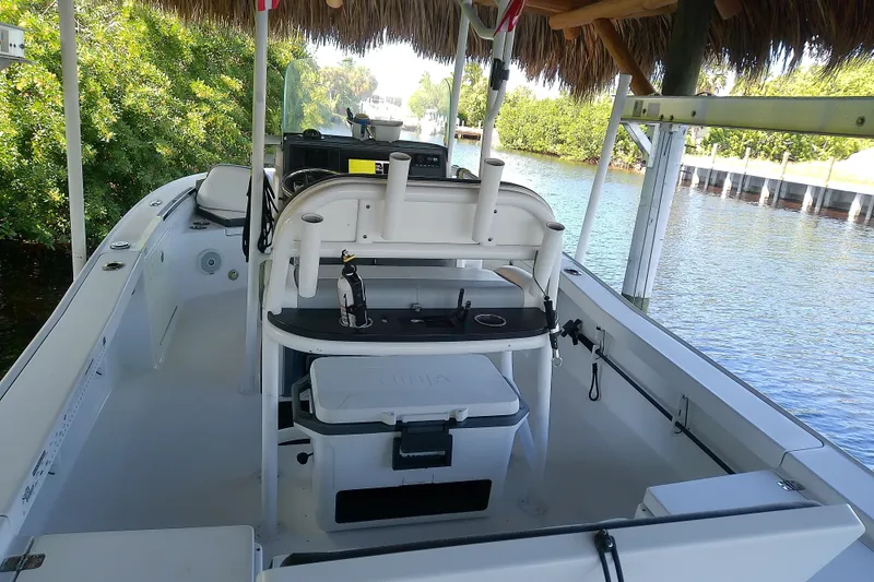 Slide: The Image of 2015 Crevalle 24 Bay boat interior with seating and storage, docked by lush greenery. - 11