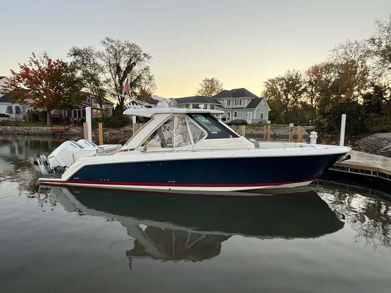 Slide: The Image of 2025 Tiara Yachts 34 LS on calm water, surrounded by autumn trees and houses. - 1