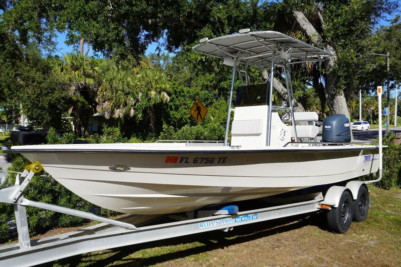 The Image of 2000 Pathfinder 2200 V boat on trailer, parked outdoors with lush greenery background. - 0