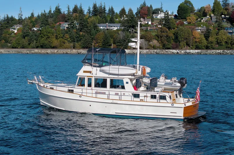 Slide: The Image of Grand Banks 46 Classic yacht cruising on blue water near a forested shoreline. - 4
