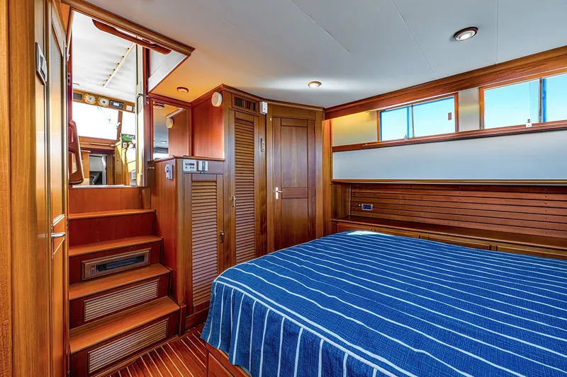 Slide: The Image of Luxurious 2002 Grand Banks 46 Classic yacht interior with wooden finishes and blue-striped bedding. - 7