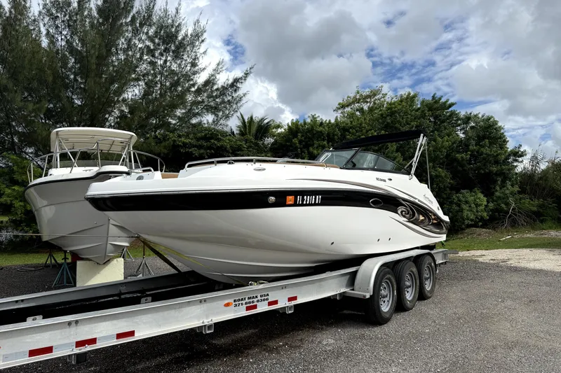 Slide: The Image of 2019 Hurricane SunDeck 2486 OB boat on a trailer, surrounded by trees and cloudy sky. - 0