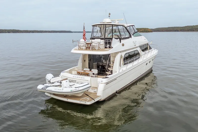 Slide: The Image of 2006 Carver 56 Voyager yacht on calm water, featuring a small boat on the deck. - 24