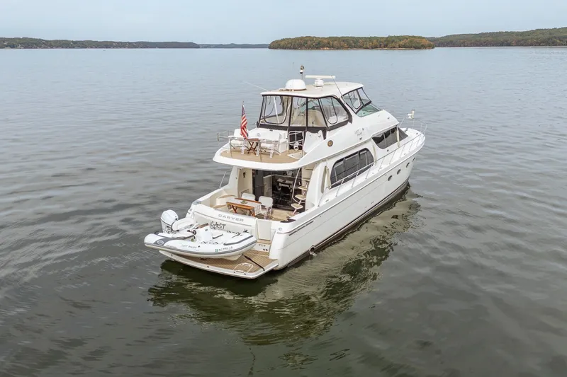 Slide: The Image of 2006 Carver 56 Voyager yacht on calm water, featuring a spacious deck and tender. - 25
