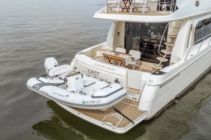 Slide: The Image of 2006 Carver 56 Voyager yacht with inflatable boat on water, featuring spacious deck and seating. - 14