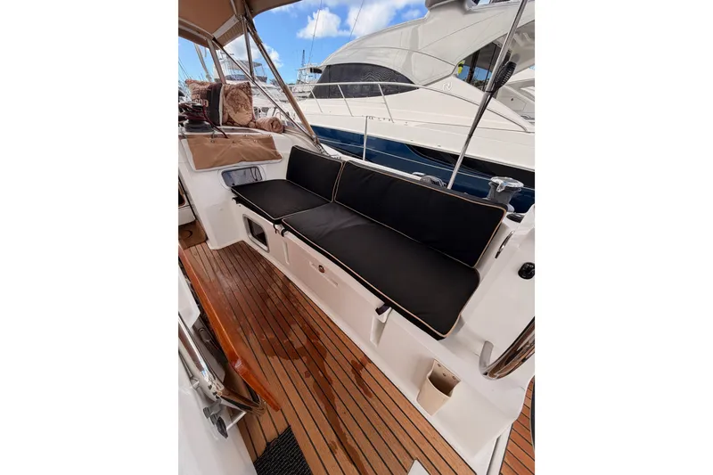 Slide: The Image of Jeanneau Sun Odyssey 469 cockpit with black cushions, teak flooring, and marina view. - 36