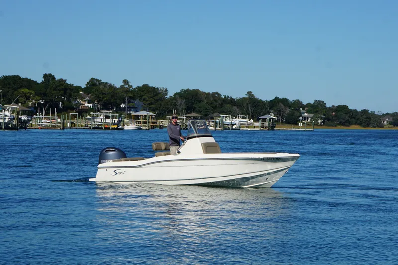 Slide: The Image of 2016 Scout 210 XSF boat cruising on a calm blue lake with scenic shoreline. - 2