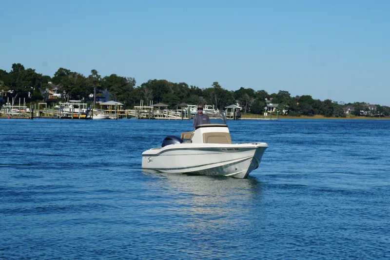 The Image of 2016 Scout 210 XSF boat cruising on a calm blue lake with shoreline in background. - 1